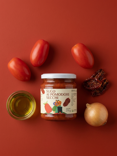 Sugo ai Pomodori Secchi Minnelea - vasetto su fondo rosso circondato dagli ingredienti