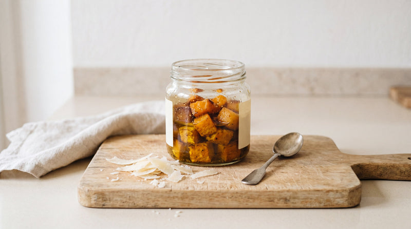Vasetto aperto di zucca tonda napoletana sott'olio su tagliere con scaglie di parmigiano