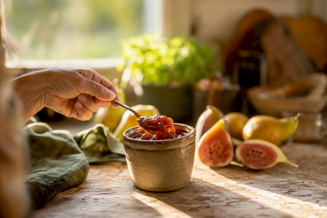 Hand, die einen Löffel aus einem Glas mit natürlicher Fruchtkonfitüre nimmt