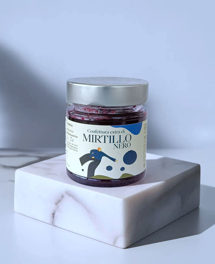 Minnelea-Glas mit Heidelbeerkonfitüre und dem Etikett Mirtillo Nero auf einem hellen Marmorblock