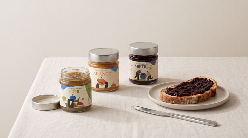 Trois pots de confiture artisanale italienne et une tartine sur nappe en lin creme